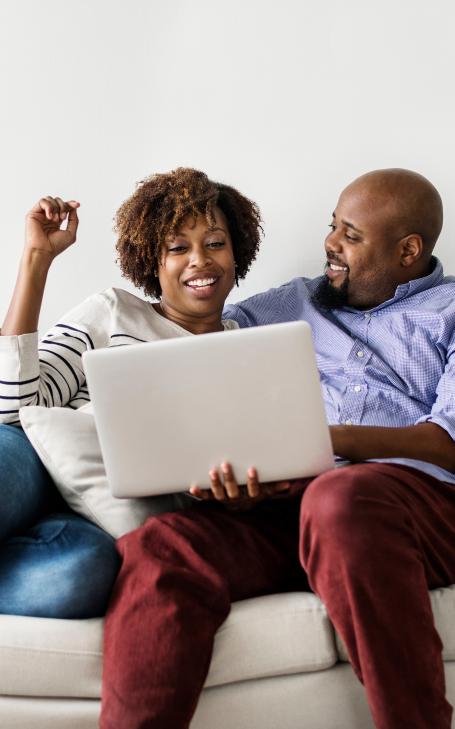 a woman and a man looking at a laptop together on a white couch