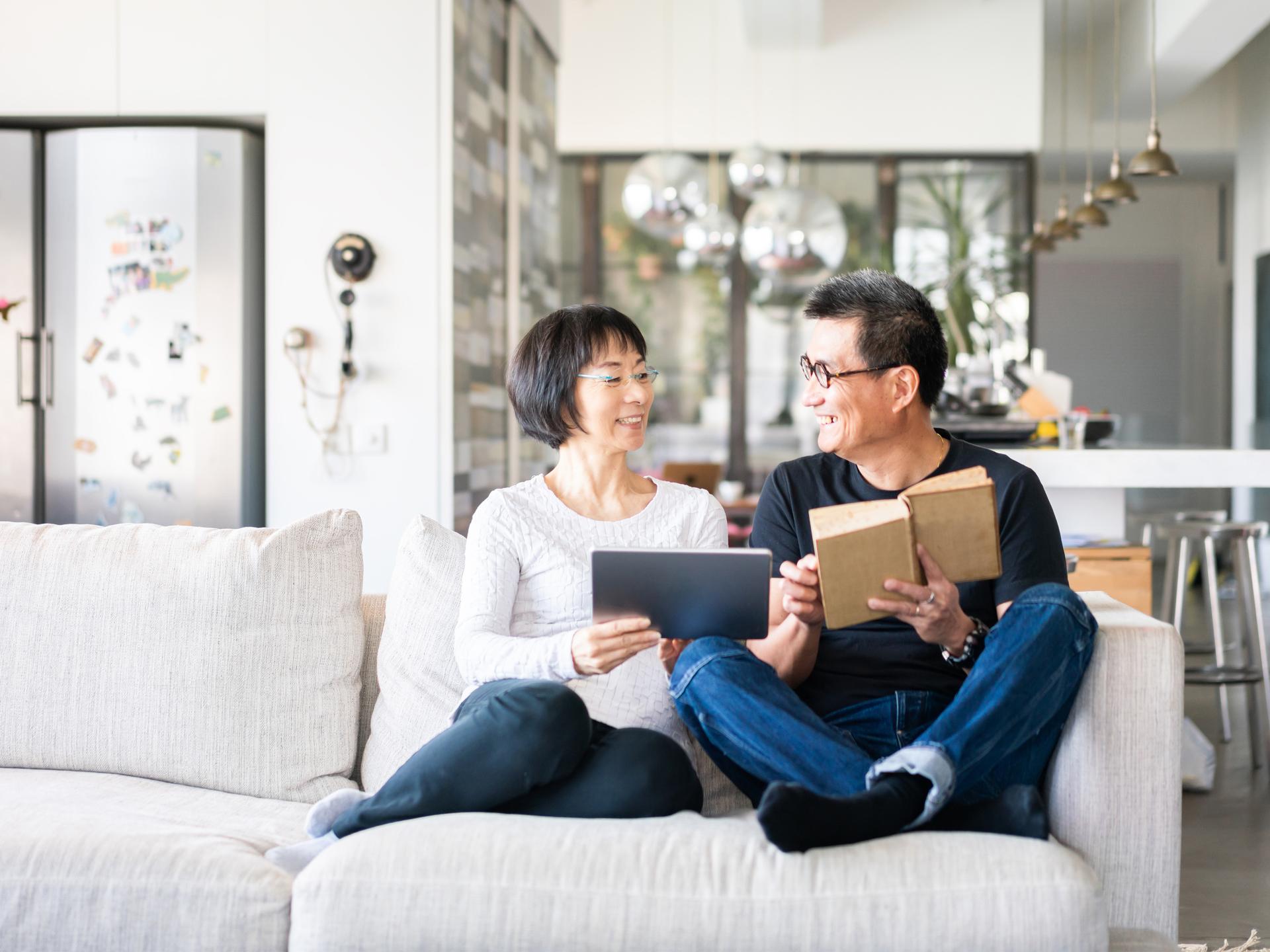 a middle aged woman and man reading on a couch in a nice house